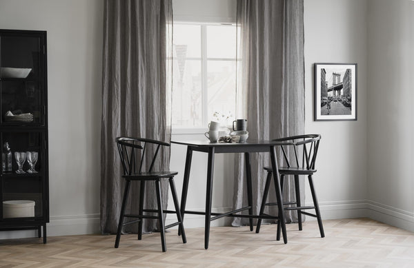 Matgrupp med svart runt bord och två pinnstolar i modern skandinavisk matsal med ljust trägolv