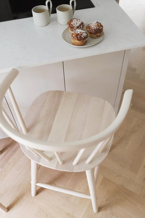 Vit träköksstol vid matbord med kaffekoppar och bakverk, skandinavisk minimalistisk design