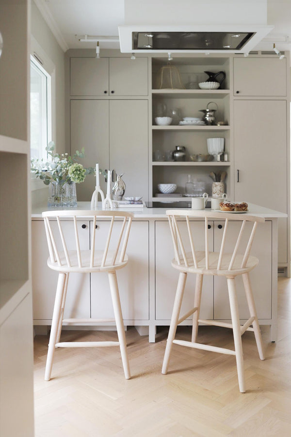 Ljust kök med vit köksö, öppna hyllor, två barstolar i trä och minimalistisk inredning