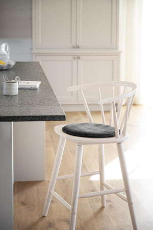 Vit barstol med spjälor i ryggstöd och grå dyna vid köksbänk med granitskiva