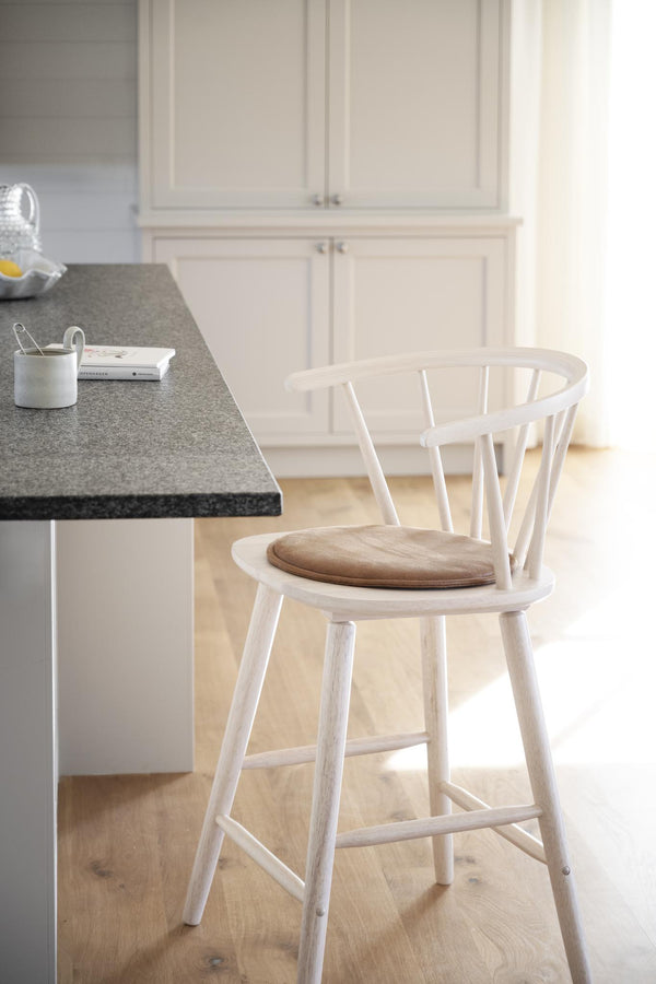 Vit barstol med spjälor och beige sittdyna vid köksbänk med grå bänkskiva