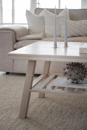 Ljust soffbord i trä med hyllplan, dekorerat med ljusstakar och prydnadsfigur i skandinavisk stil