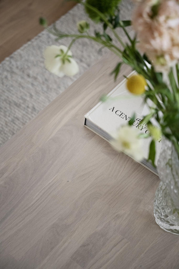 Doftljus A Century of med vita blommor i glasvas på trägolv med grå textilier i bakgrunden