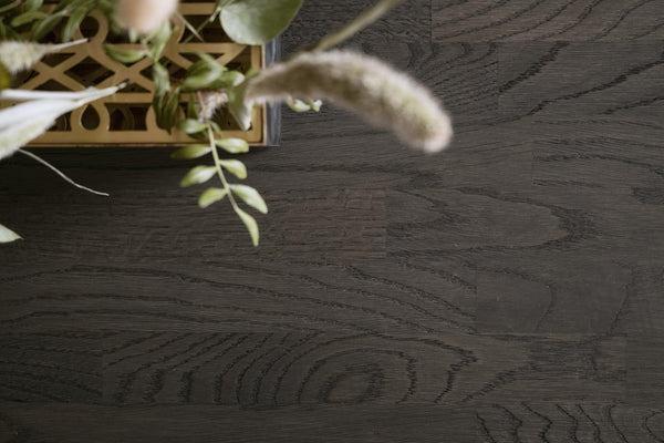 Mörkt trägolv med synlig ådringsmönster och grön växt i korg i hörnet