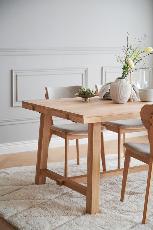 Matbord i ljust trä med matchande stolar och grå klädda dynor i skandinavisk matsalsmiljö