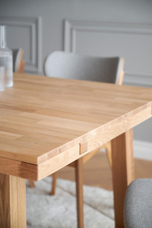Massivt matbord i ek med synlig träåder och snickeridetlajer, omgivet av grå stolar i modern skandinavisk stil