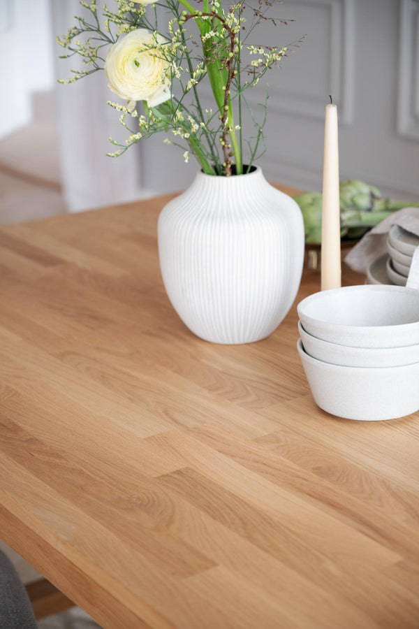 Vit ribbad vas med blommor på träbord bredvid stearinljus och vita skålar i skandinavisk stil