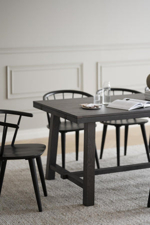 Svart matbord i trä med matchande stolar i modern skandinavisk design, stylat med bok och glasvaror