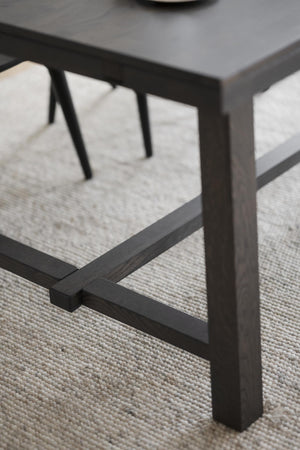 Närbild på svarta träben till soffbord med elegant design och korsformad detalj på ljus matta