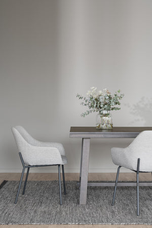 Matbord i grått trä med två vita stolar och vas med eukalyptus på grå matta