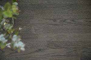 Mörkgrått trägolv med synlig trästruktur och gröna växtdetaljer i hörnet