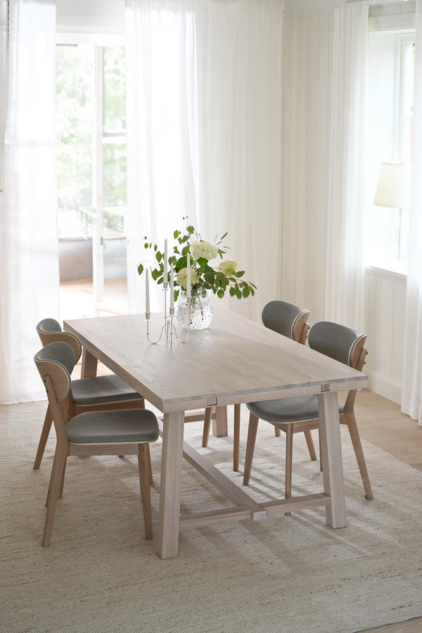 Matgrupp med ljust trä och gråa stoppade stolar i ljust skandinaviskt matrum med vita gardiner