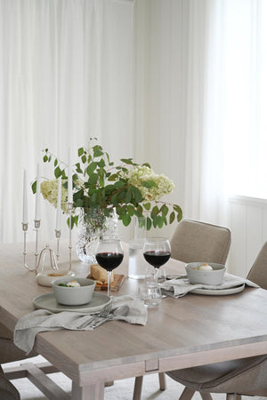 Elegant dukat matbord med vita hydrangeor, ljusstakar, vinglas och grå keramikskålar i naturlig stil