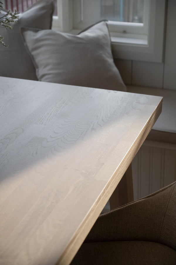 Ljust trä matbord med synlig trästruktur i modern skandinavisk matsal med gråa stolar och fåtölj