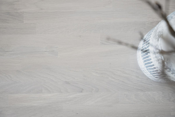 Ljust trägolv i ek med synlig struktur och dekorativ vas i hörnet