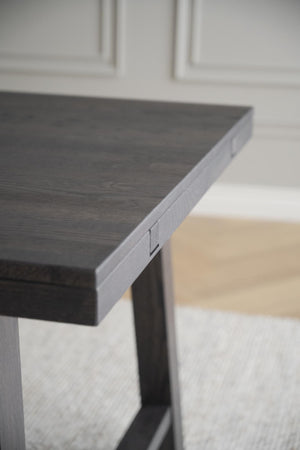 Närbild på hörnet av ett grått träbord med trästruktur och svarta ben mot ljus bakgrund