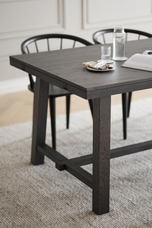 Svart matbord i trä med rustik design, tjocka ben och förstärkta sidor, med glasvatten och stolar i bakgrunden