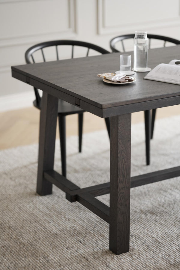 Svart matbord i trä med rustik design, tjocka ben och förstärkta sidor, med glasvatten och stolar i bakgrunden