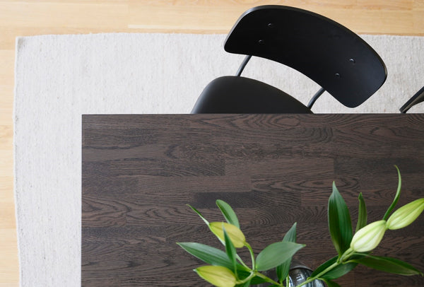 Mörkt trädiningbord med svart stol och vita liljeblommor ovanifrån