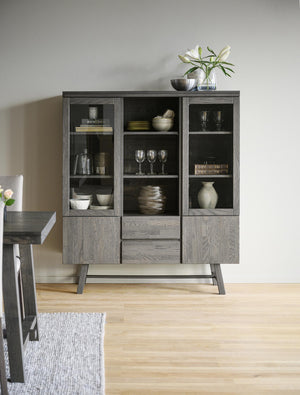 Grå vitrinskåp i modern design med glasdörrar, hyllor och lådor, inrett med porslin och dekorationer