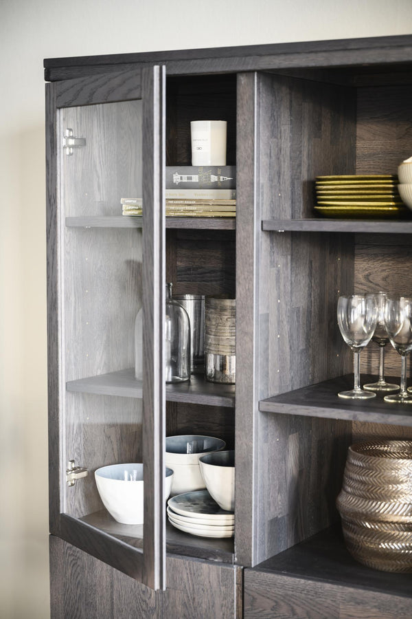 Vitrinskåp i mörkgrå ek med glasdörrar och hyllplan med porslin, glas och dekorativa föremål