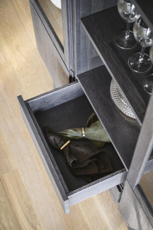 Öppen låda i mörkt trä med förvarade napkins och servetter, del av serveringsskåp med vinglas ovanpå