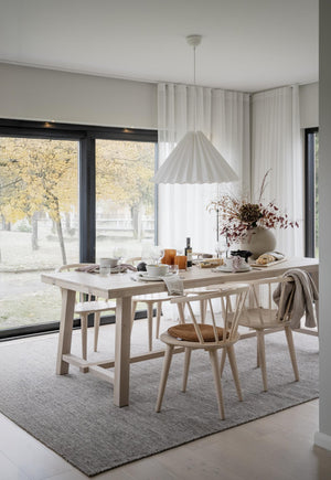 Ljus matplats med träbord, designstolar och vit taklampa framför stora fönster med höstvy