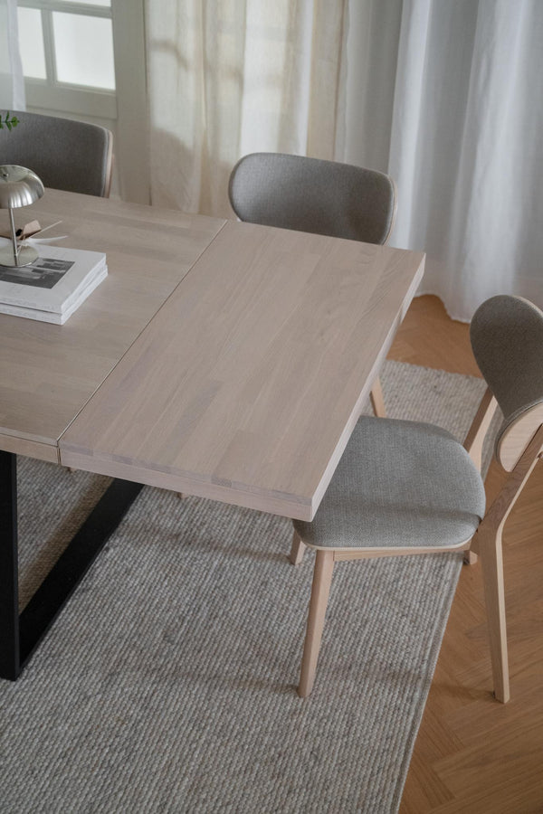 Ljust matbord i trä med grå stoppade stolar på en ljusgrå matta i modernt matrum