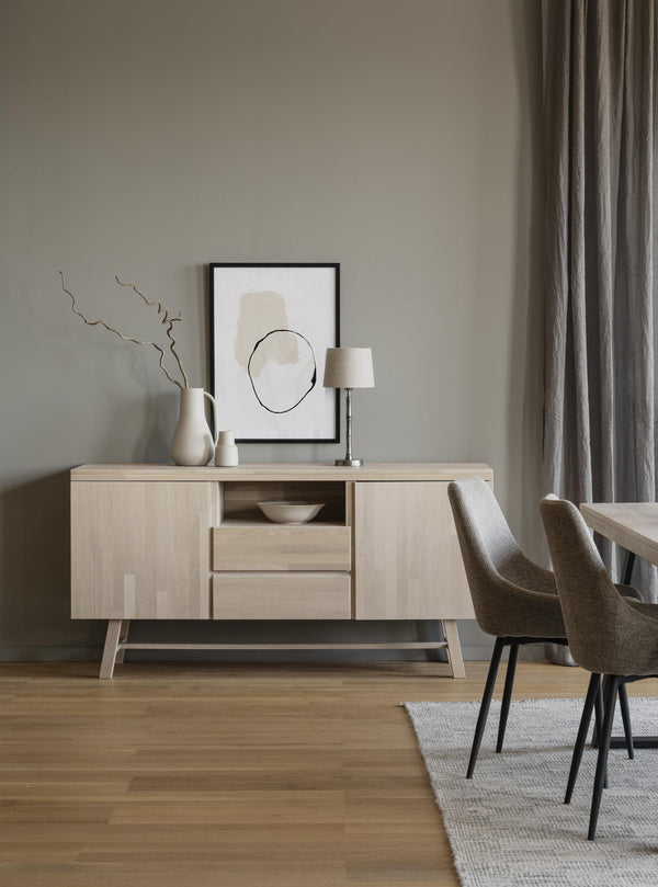 Ljust sideboard i trä med två skåp och lådor, dekorerat med vas, tavla och lampa i minimalistisk matsal
