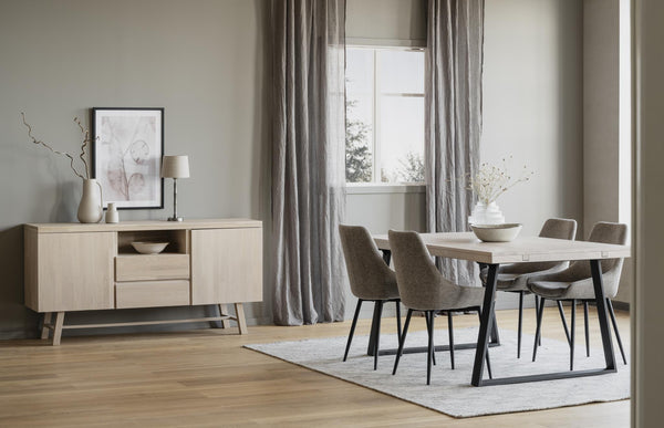 Matgrupp med bord och stolar i skandinavisk stil bredvid sideboard i ljust trä, grå gardiner och parkettgolv