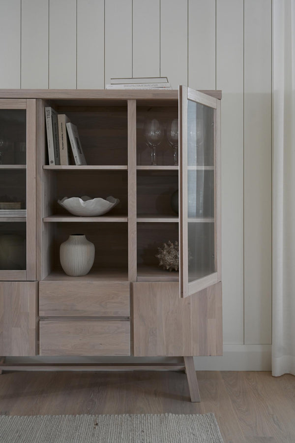 Vitrinskåp i ljust trä med glashyllor, öppna fack och lådor, dekorerat med keramik och böcker