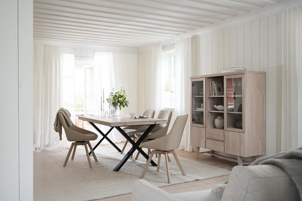 Matbord med kryss-ben och beige stolar i skandinavisk matsal med vitrinskåp
