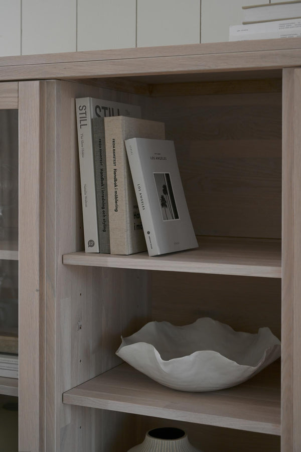 Bokhylla i ljust trä med böcker och dekorativ keramikskål i minimalistisk skandinavisk stil