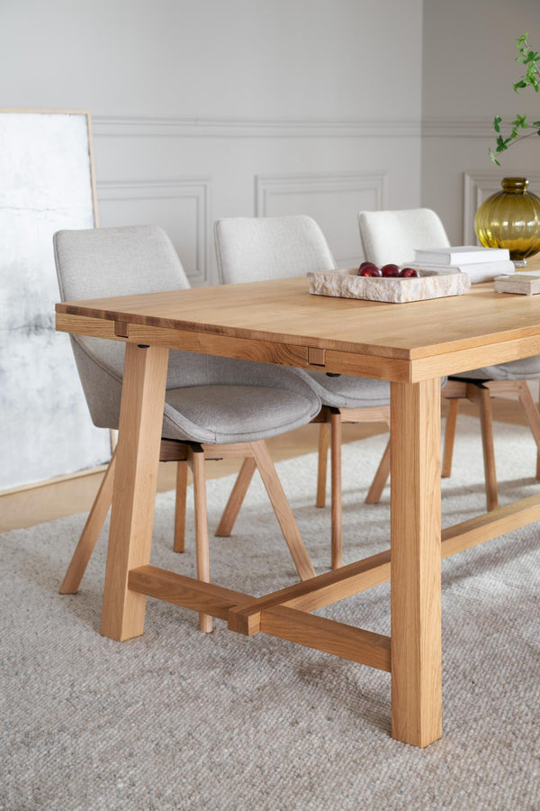 Matbord i ek med stående konstruktion och grå stoppade stolar i skandinavisk design