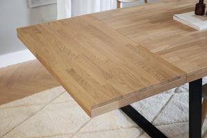 Utdragbar matbord i ljus ek med synliga åringar och svarta metallben på vit matta