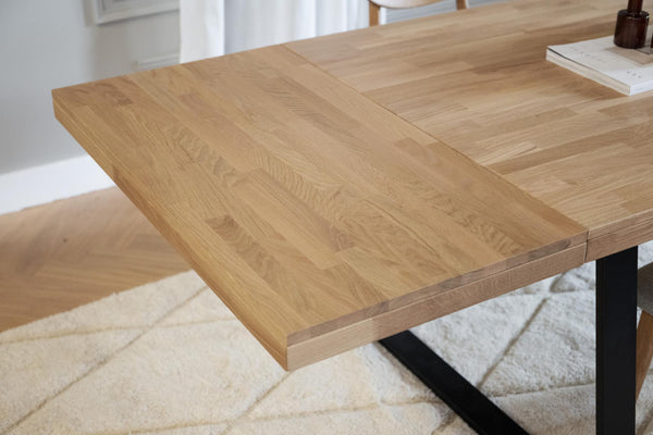 Utdragbar matbord i ljus ek med synliga åringar och svarta metallben på vit matta