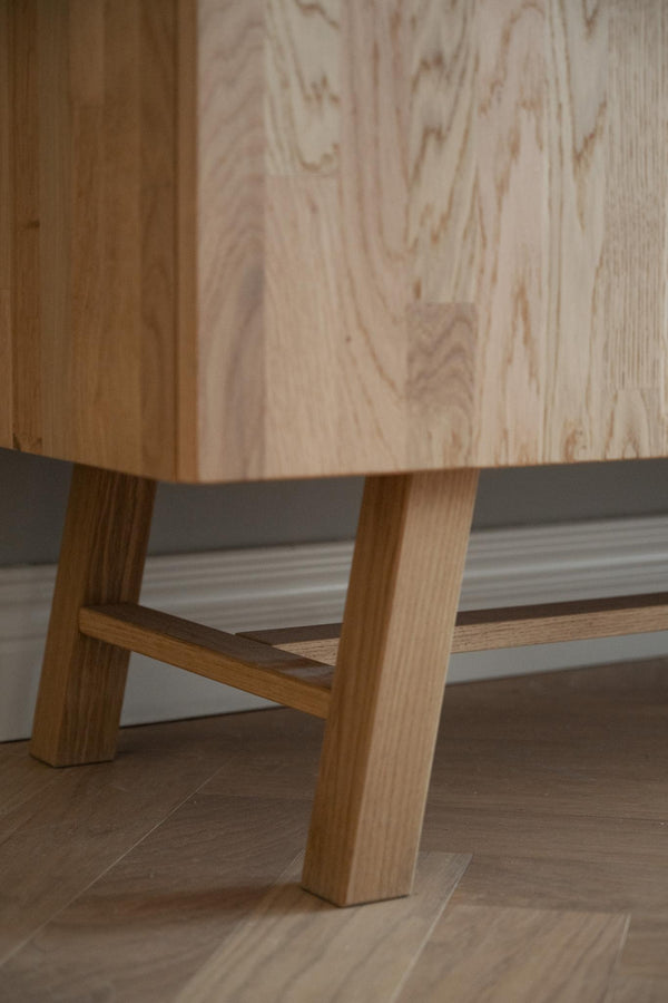 Närbild av möbelfötter i ljus ek med träskena mot trägolv och plywoodvägg