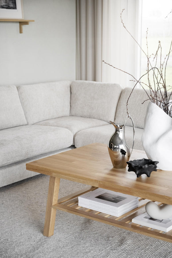 Ljust vardagsrum med beige soffa och soffbord i ek med hylla, dekorerat med vaser och böcker