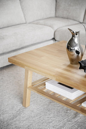 Soffbord i ljust trä med hylla, dekorerat med silverkanna och böcker, framför grå soffa