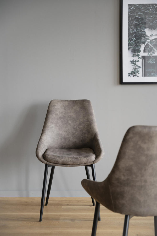 Gråbrun matstol i sammet med svarta ben på trägolv mot vit vägg med tavla