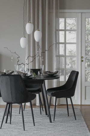 Svart matgrupp med fyra sammetsstolar runt matbord i modern skandinavisk matsal med vita taklampor