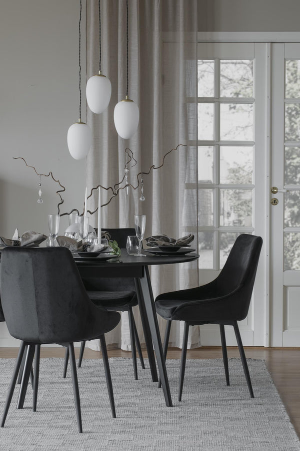 Svart matgrupp med fyra sammetsstolar runt matbord i modern skandinavisk matsal med vita taklampor