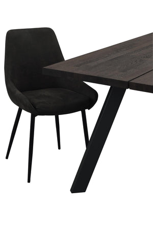 Svart sammetsstol vid mörkbrunt matbord med V-formade ben i modern skandinavisk design