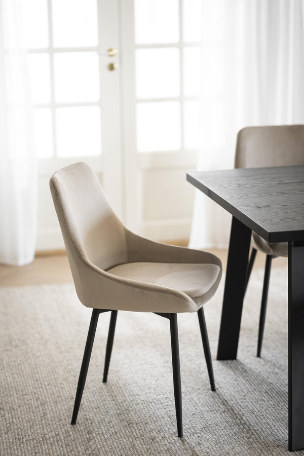 Beige matstol med svarta ben vid matbord i modernt hem med ljusinsläpp från fönster