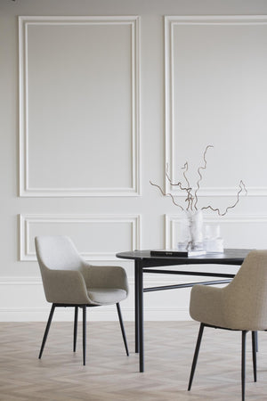 Moderna matstolar i beige tyg med svarta ben vid runt matbord i minimalistisk matsal med tavelramar på väggen