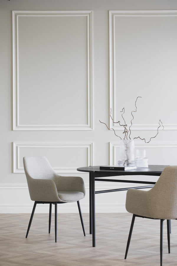 Moderna matstolar i beige tyg med svarta ben vid runt matbord i minimalistisk matsal med tavelramar på väggen