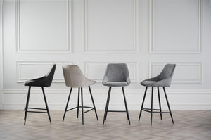 Fyra moderna barstolar i svart, beige och grå mot vit vägg med spegelpaneler