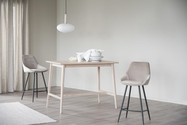 Matbord i ljust trä med hylla, två grå barstolar och vit taklampa i minimalistisk matsal