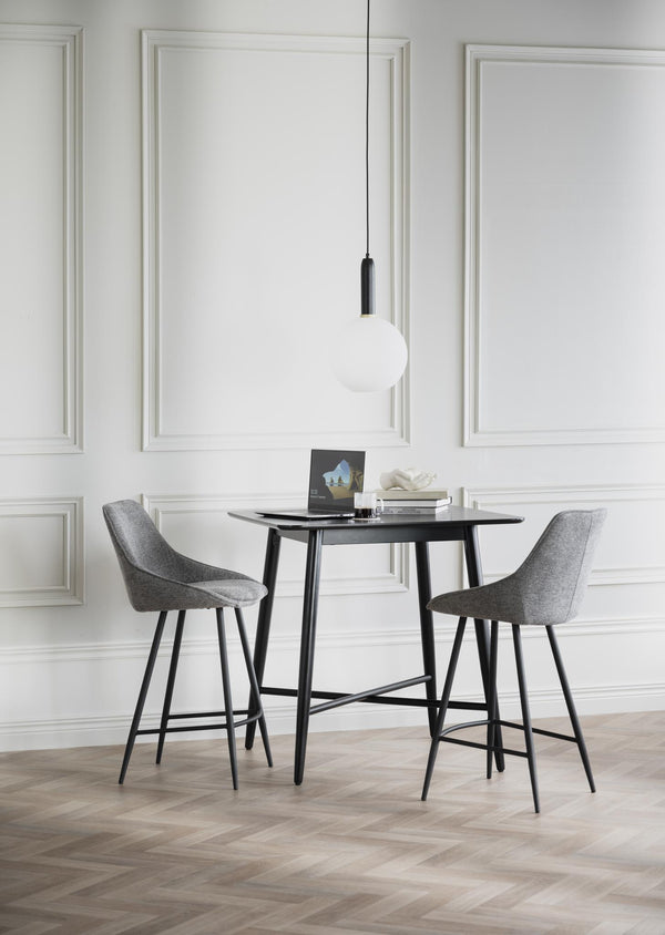 Grå barstolar vid svart barbord i modernt rum med vit väggpanel och designlampa