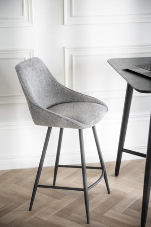 Grå stoppad barstol med metallben vid svart barbord mot vit panelvägg